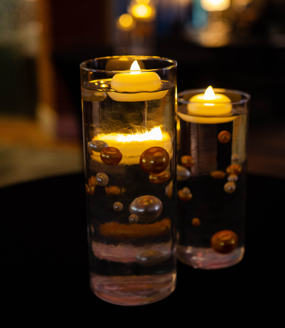 Event decorations of floating candles in glass cylinders are shown atop black tablecloths