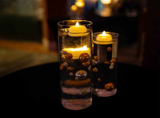 Event decorations of floating candles in glass cylinders are shown atop black tablecloths