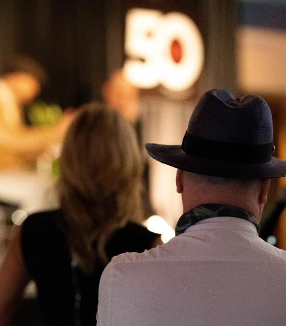 The audience listens intently at the JRT agency in an event photo of lighted stage and 50th logo