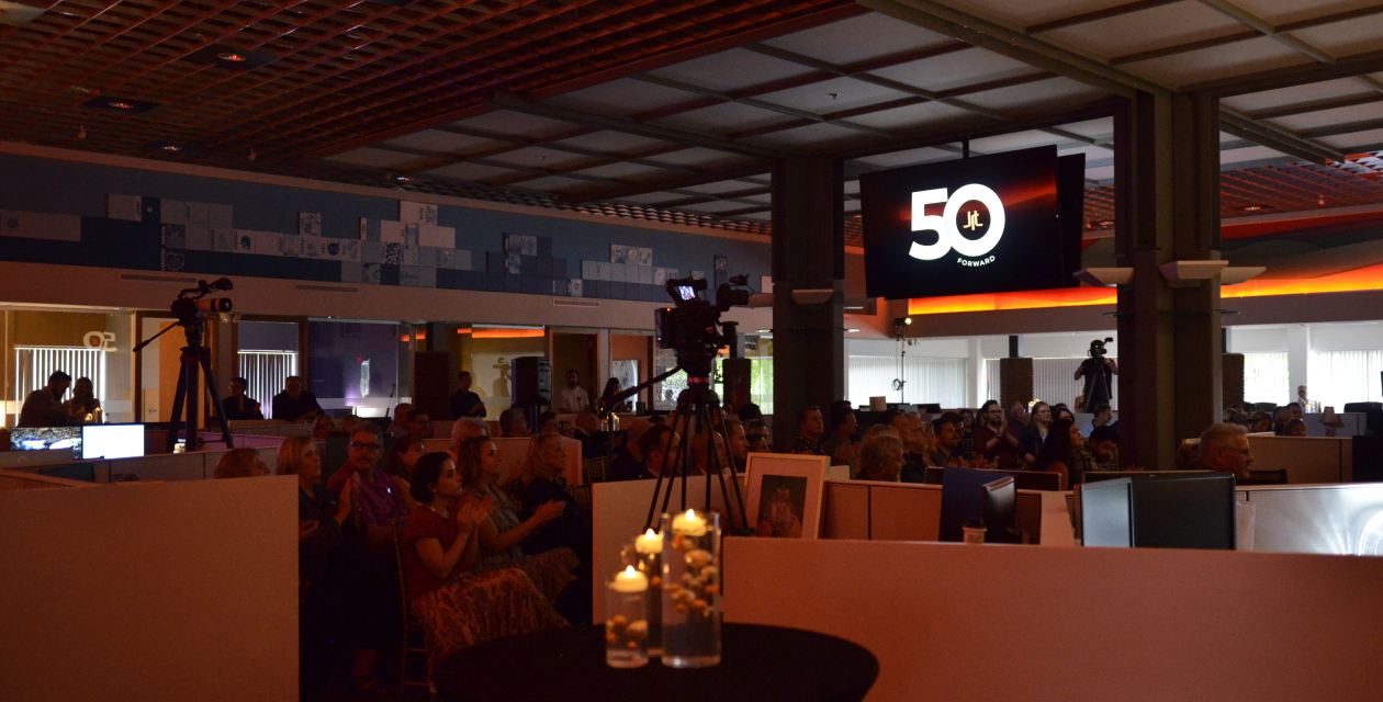 The audience sits under dim lighting, listening intently as Nikola Danaylov presents at the JRT agency's 50th anniversary event