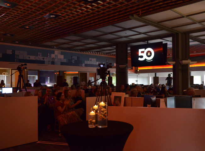 The audience sits under dim lighting, listening intently as Nikola Danaylov presents at the JRT agency's 50th anniversary event