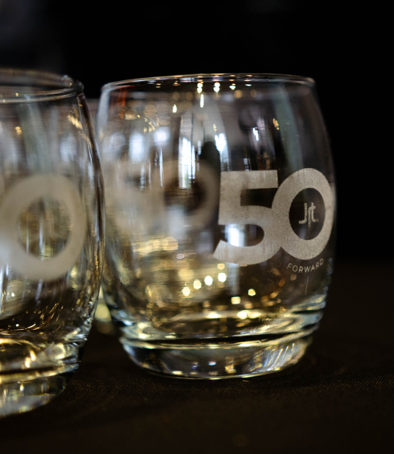 Custom wine glasses with engraving of the JRT agency's 50 Forward logo are shown on a black table cloth