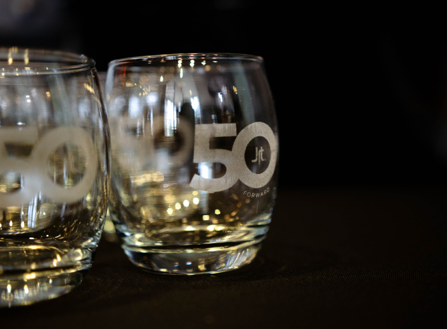 Custom wine glasses with engraving of the JRT agency's 50 Forward logo are shown on a black table cloth