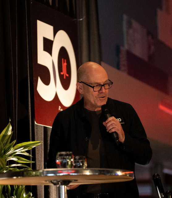 Mark Bellissimo of the JRT agency in an event photo of lighted stage and 50th logo