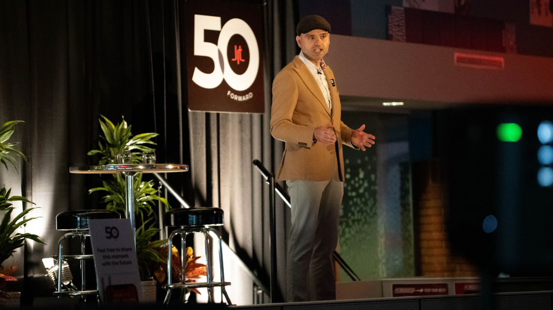 Nikola Danaylov of Singularity speaks at the JRT agency in a 50th anniversary event photo of lighted stage and 50th logo