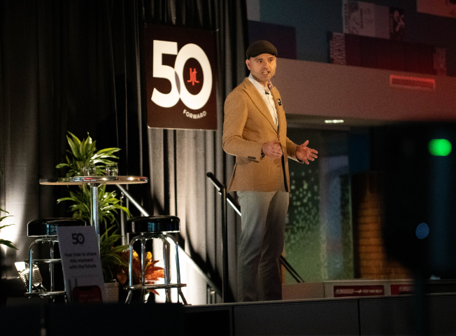 Nikola Danaylov of Singularity speaks at the JRT agency in a 50th anniversary event photo of lighted stage and 50th logo